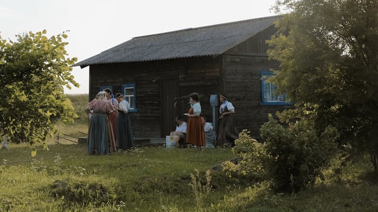 Group of people in traditional attire gathered outside a rustic cabin in Karelia's countryside.
