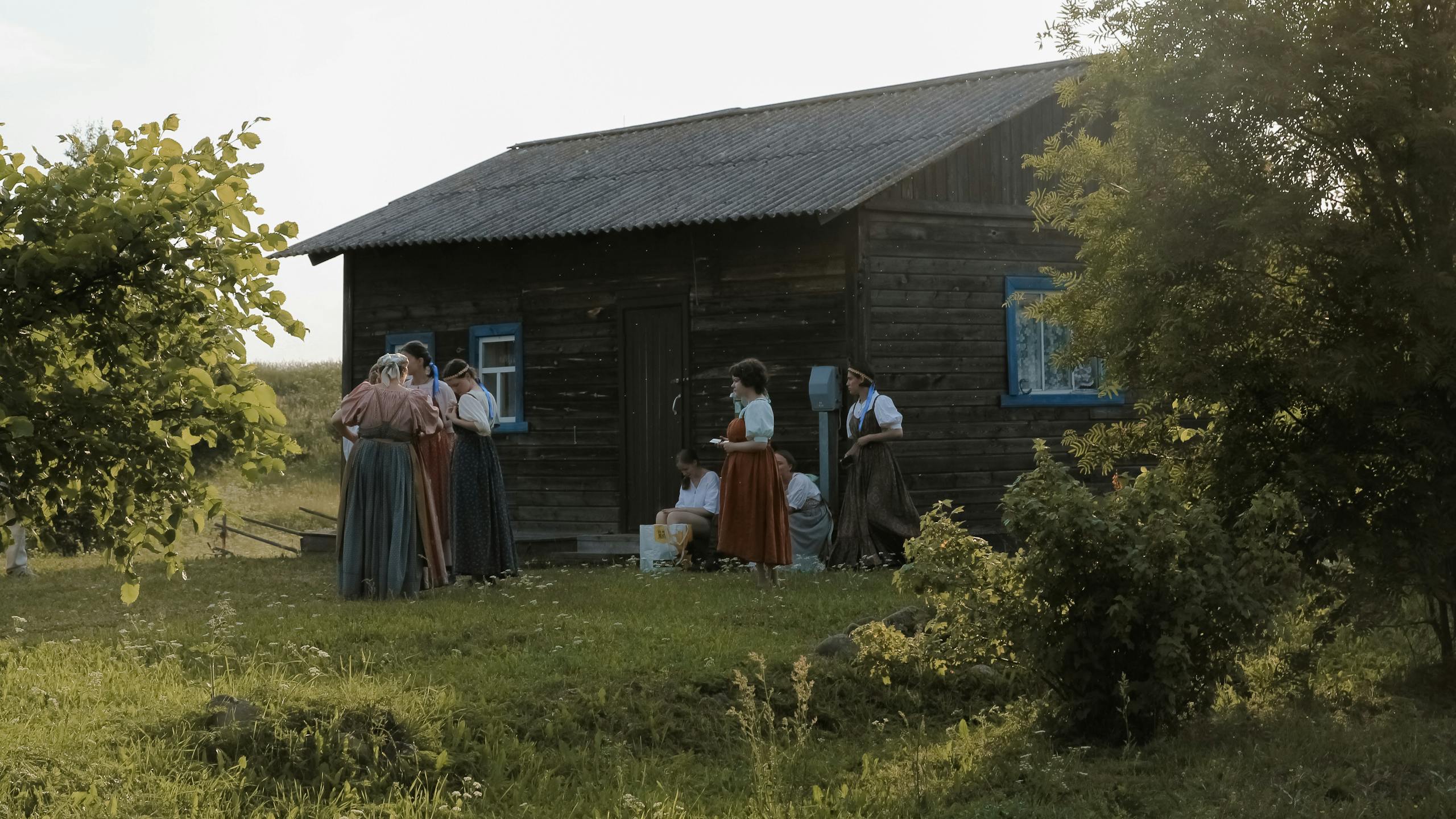 Group of people in traditional attire gathered outside a rustic cabin in Karelia's countryside.