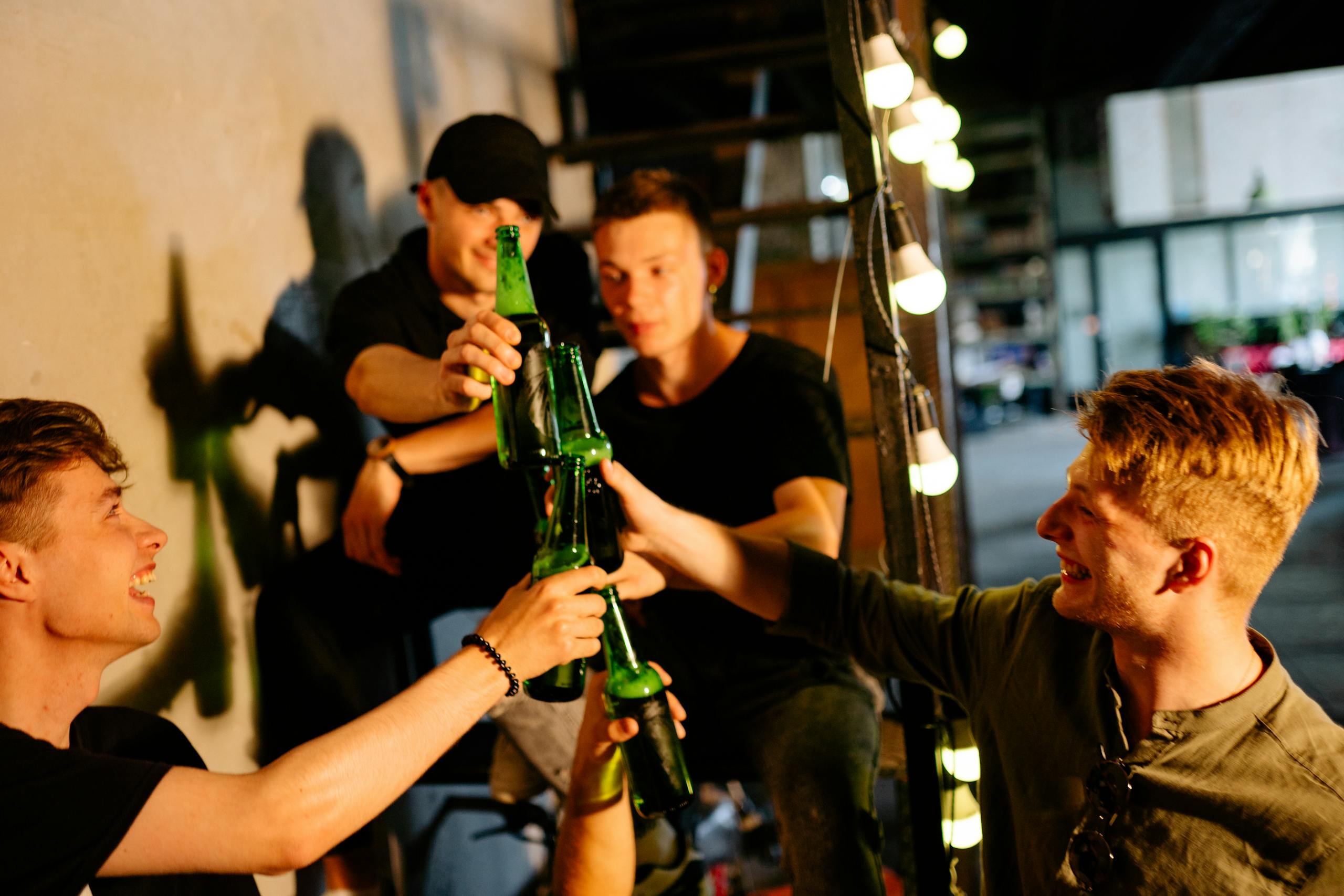 Group of young friends enjoying a drink together, toasting with bottles indoors.