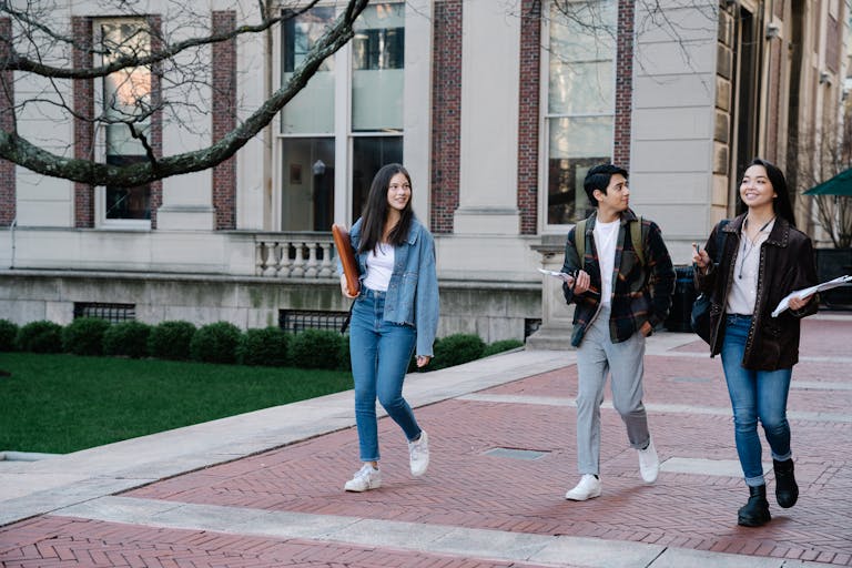 Group of young students walking on campus sidewalk on a bright day, showcasing casual university life.