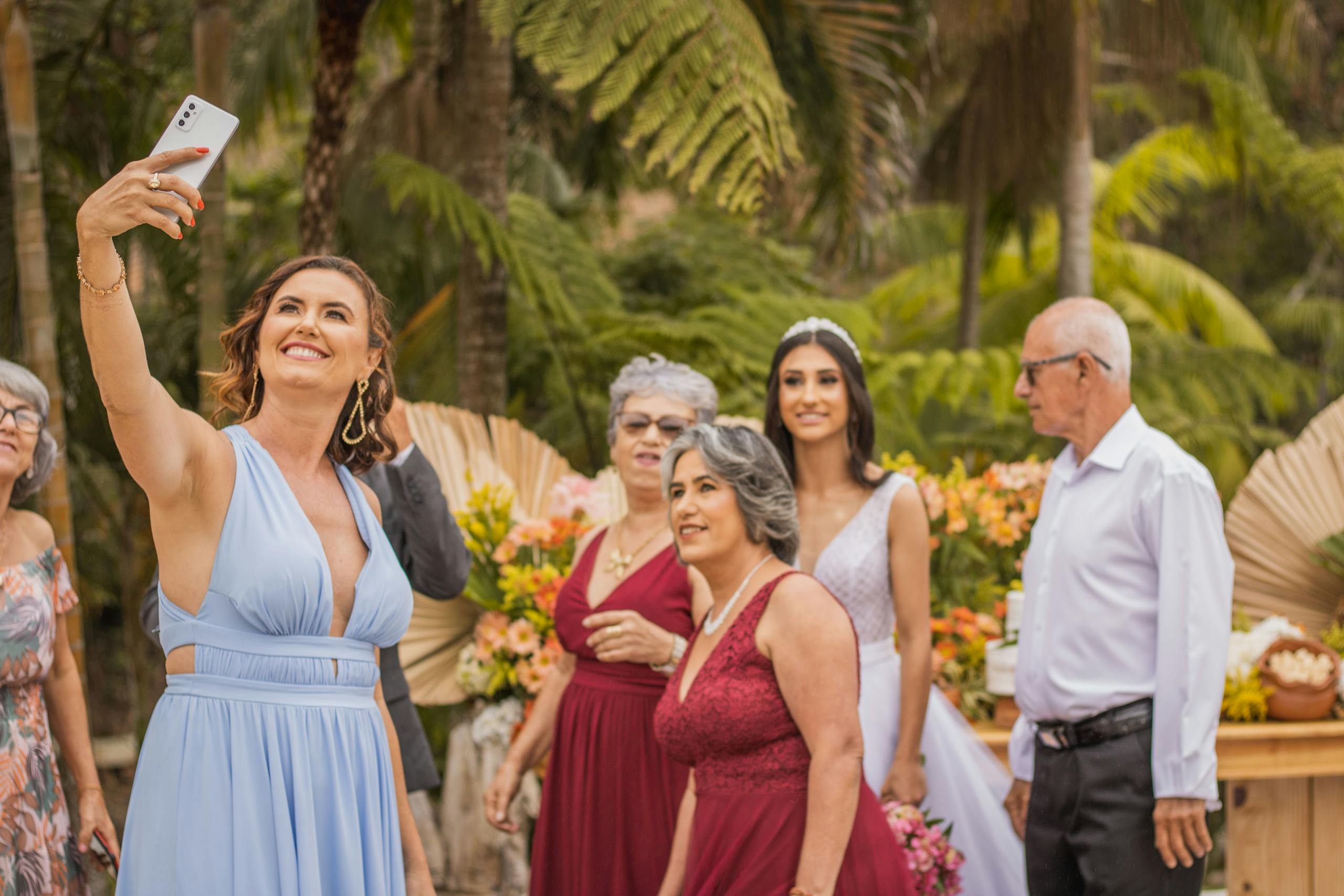 Guests and bride enjoying an outdoor wedding reception while capturing a group selfie for memories.