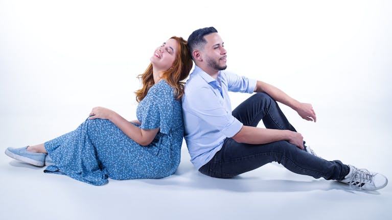 Happy couple sitting back to back in a studio, embracing togetherness and joy.