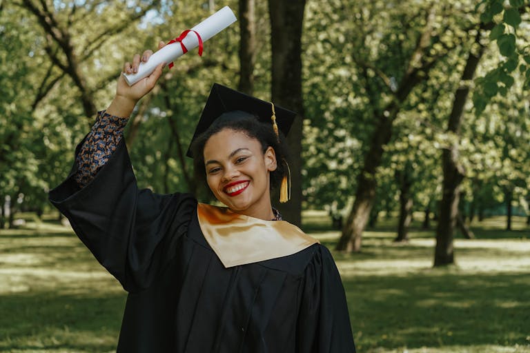 Happy graduate celebrating outdoors, holding diploma with a smile.