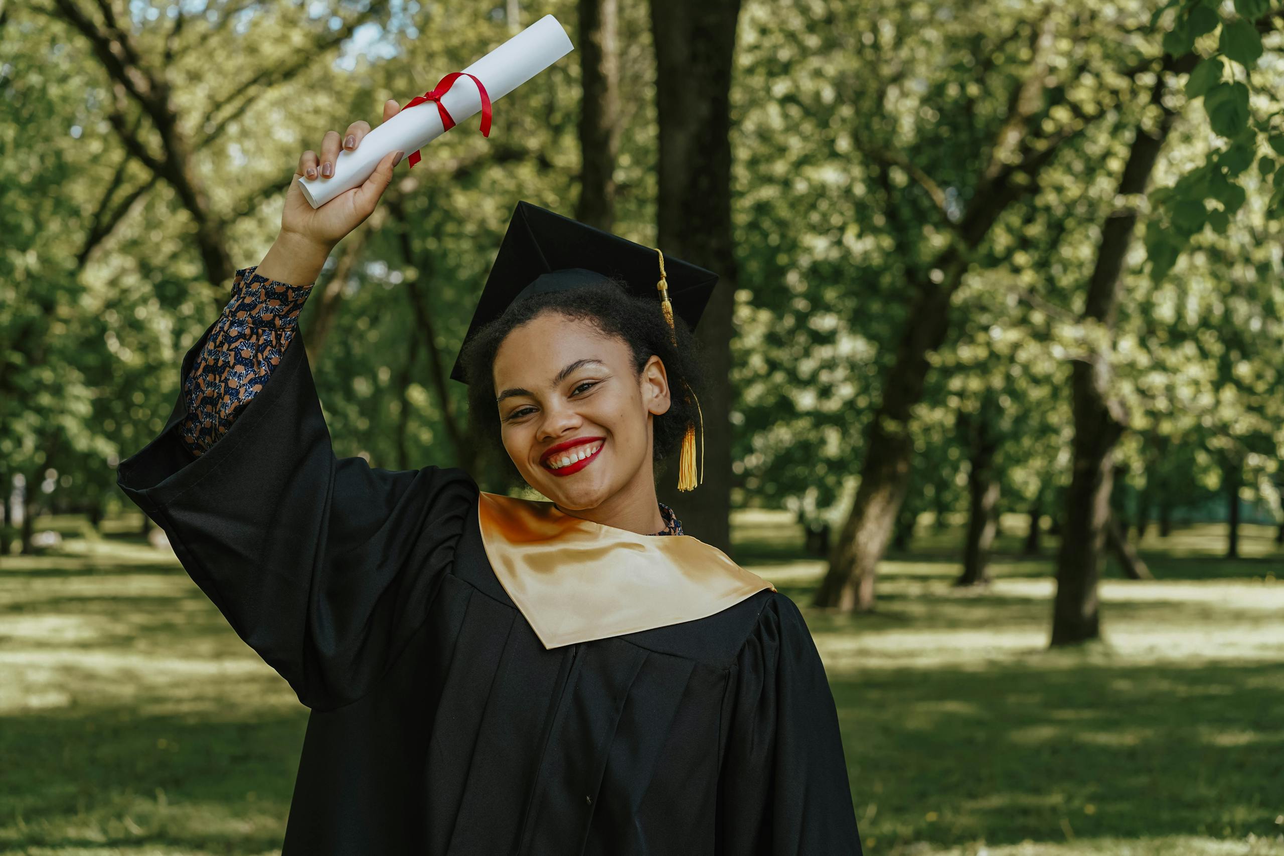Happy graduate celebrating outdoors, holding diploma with a smile.