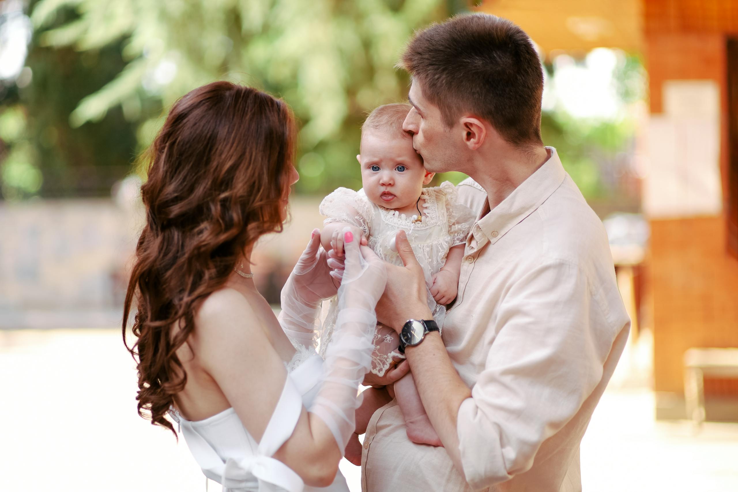 Happy young parents lovingly embracing their baby in a sunny outdoor setting.