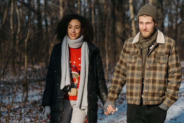Interracial couple enjoying a winter walk, radiating love and happiness in festive attire.