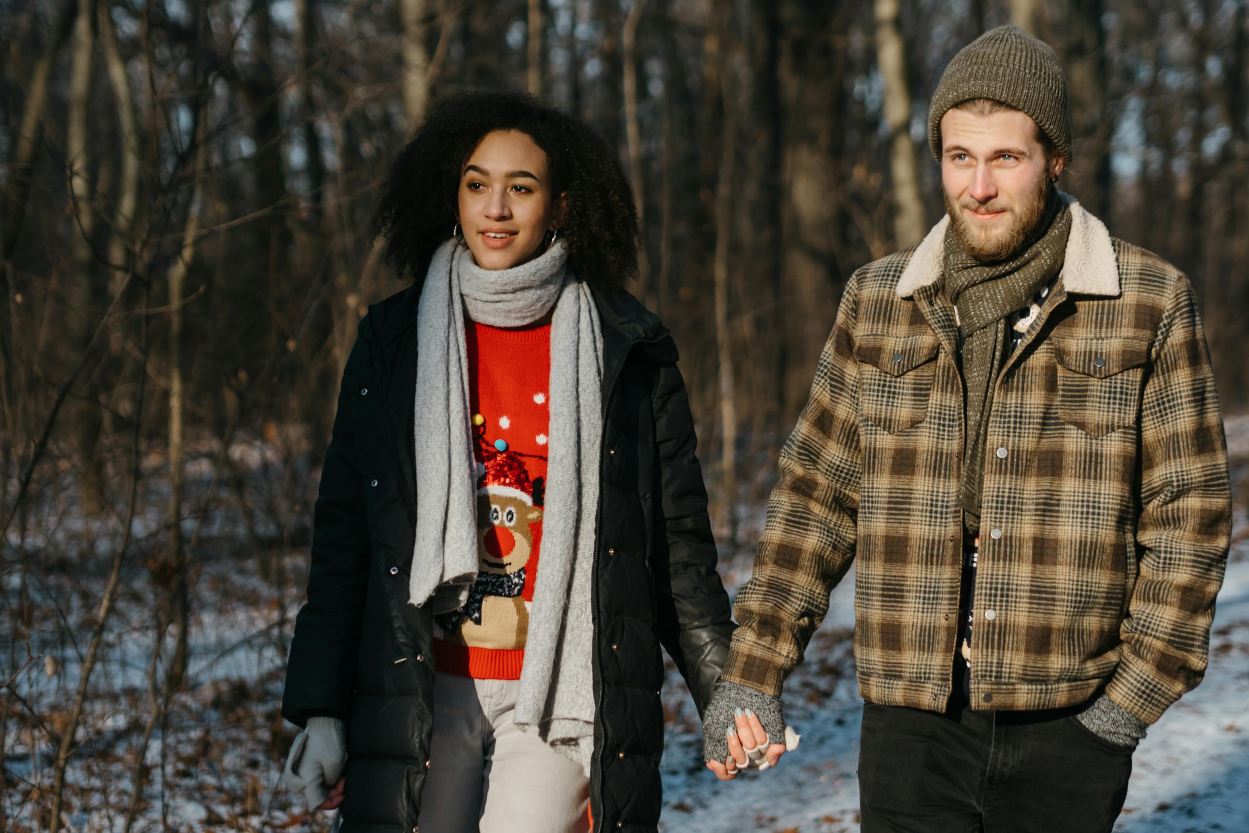 Interracial couple enjoying a winter walk, radiating love and happiness in festive attire.