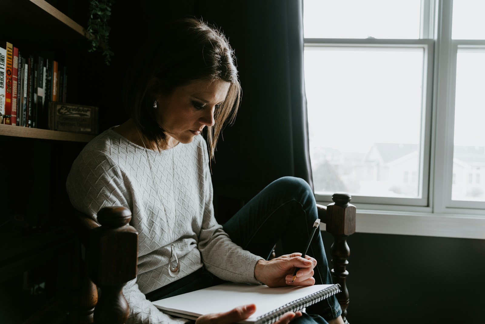 A woman sitting in a chair writing in a notebook.