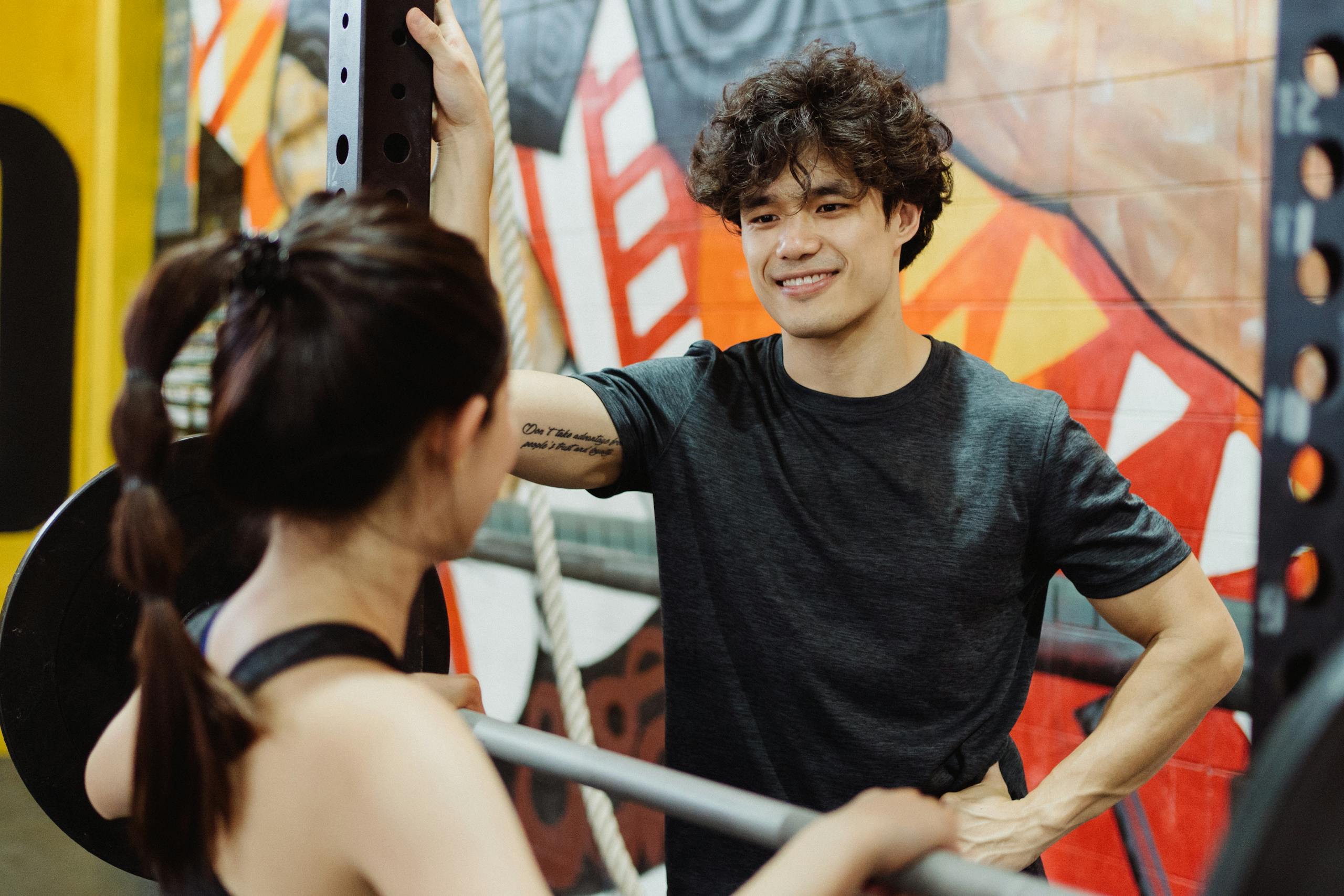 Man and woman engage in a friendly conversation in a gym with colorful graffiti walls.