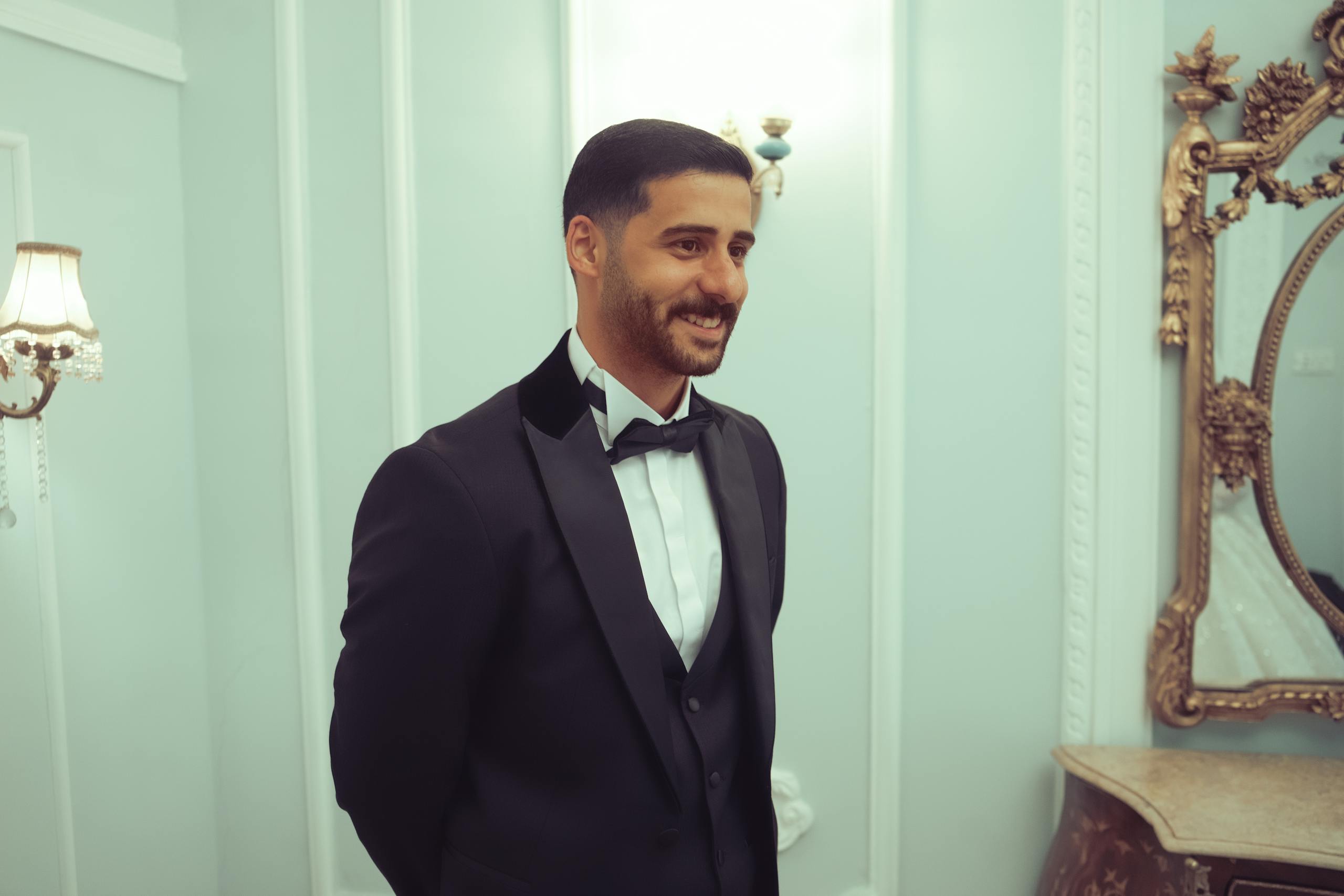 Man in a tuxedo smiling indoors in a luxurious, ornate setting in Baghdad.