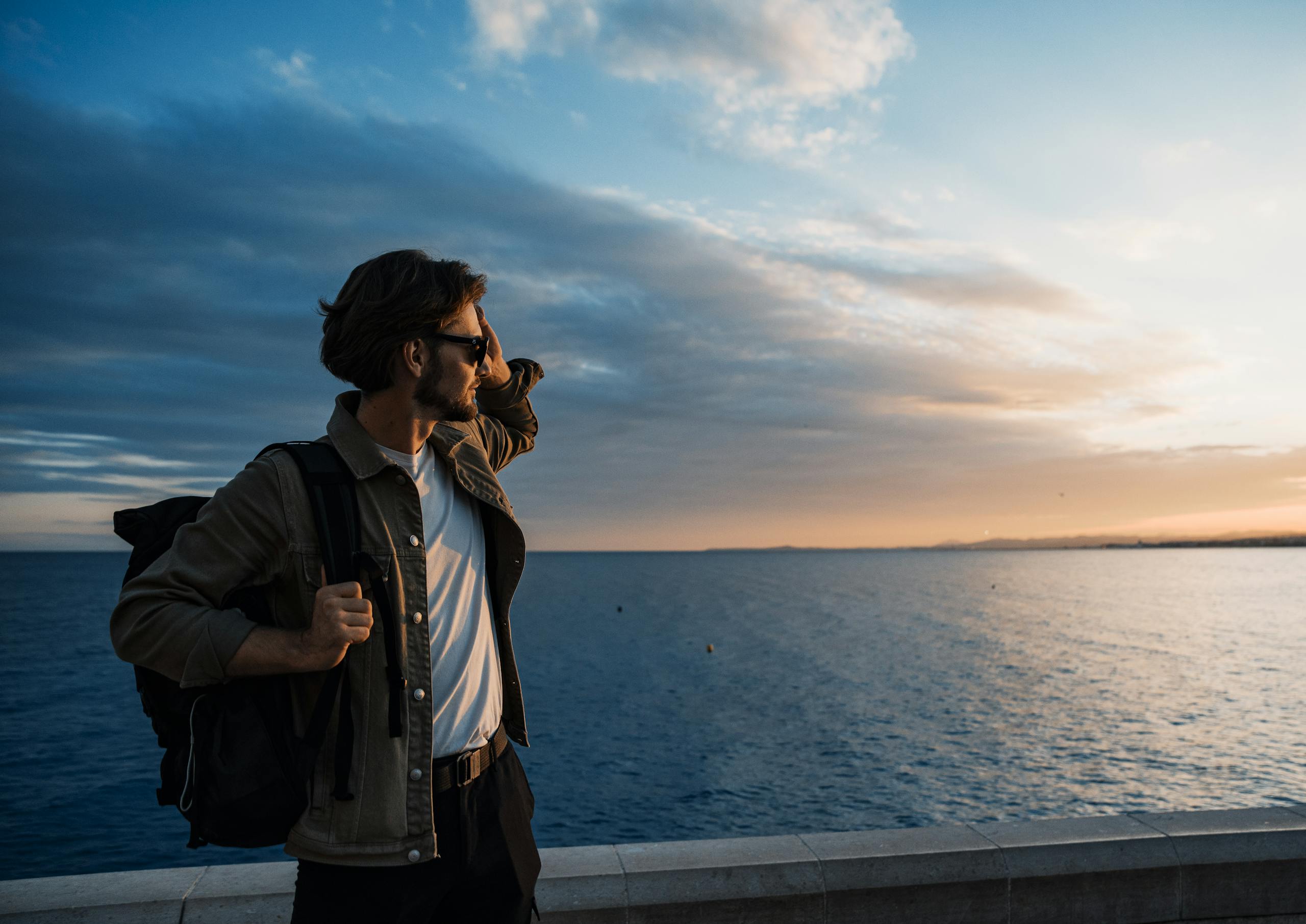 Man with a backpack gazing at the sunset over the sea in Nice, France. Perfect for travel inspiration.