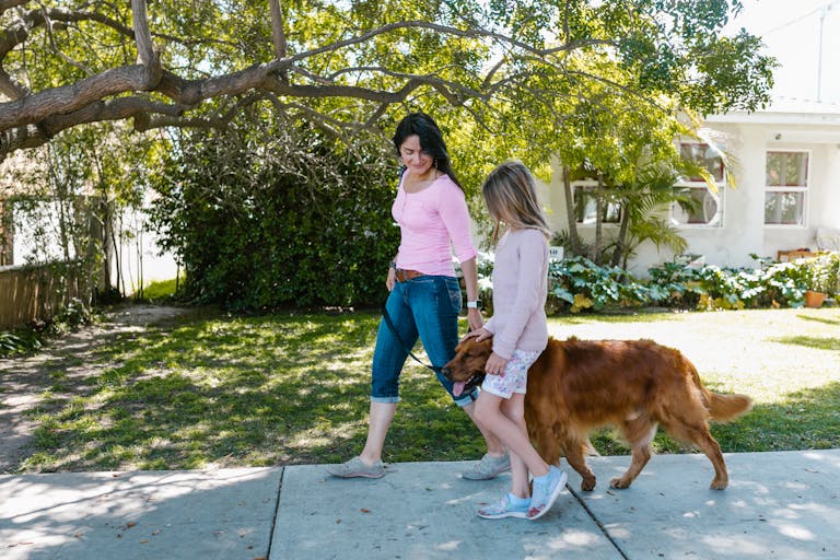 Mother and daughter enjoying a walk with their dog on a sunny day in a suburban neighborhood.
