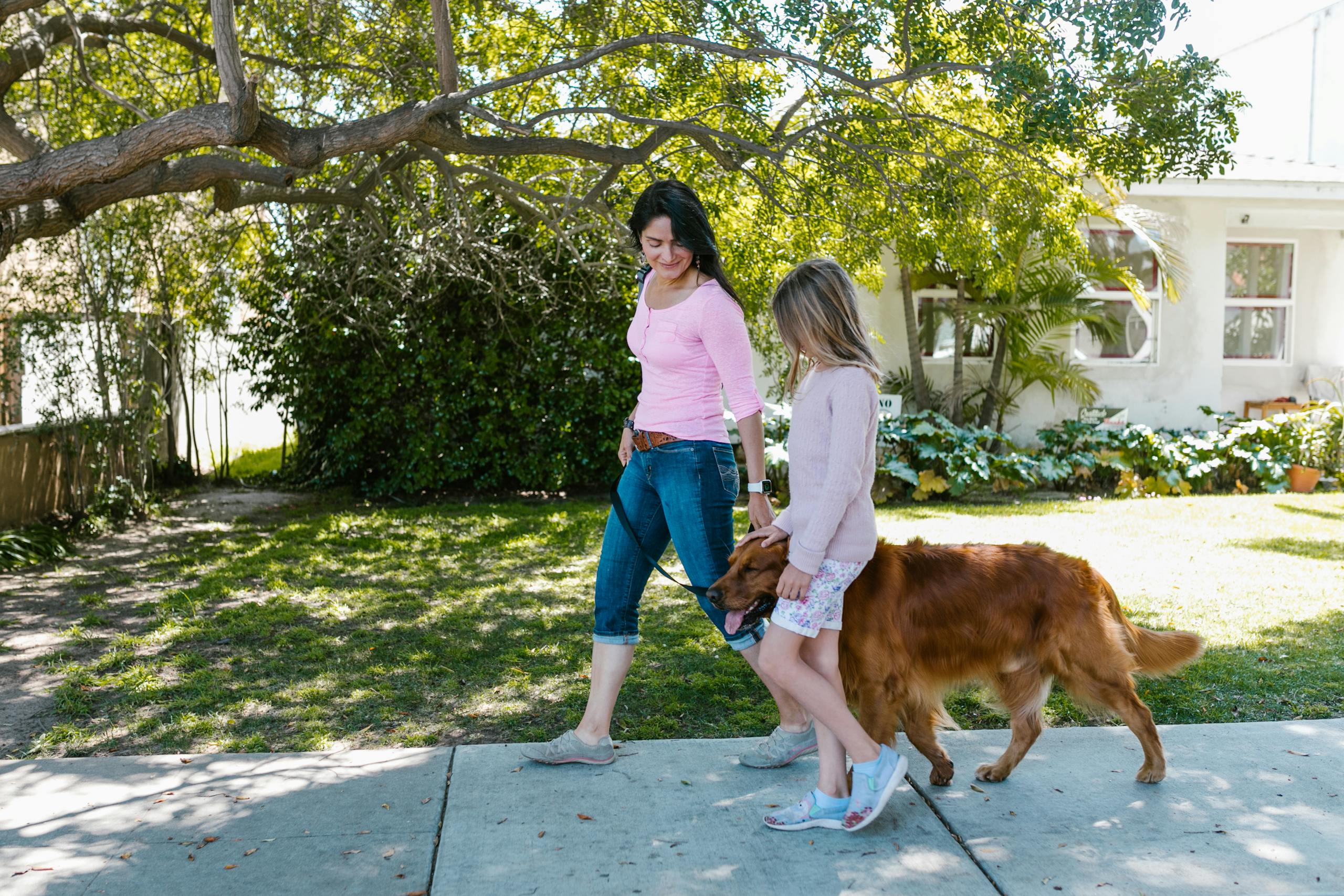 Mother and daughter enjoying a walk with their dog on a sunny day in a suburban neighborhood.