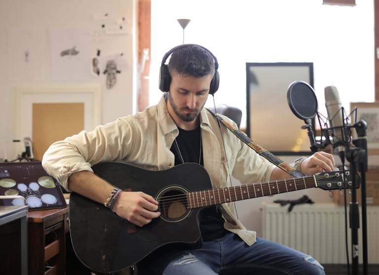 Musician adjusting guitar strings in modern recording studio environment.