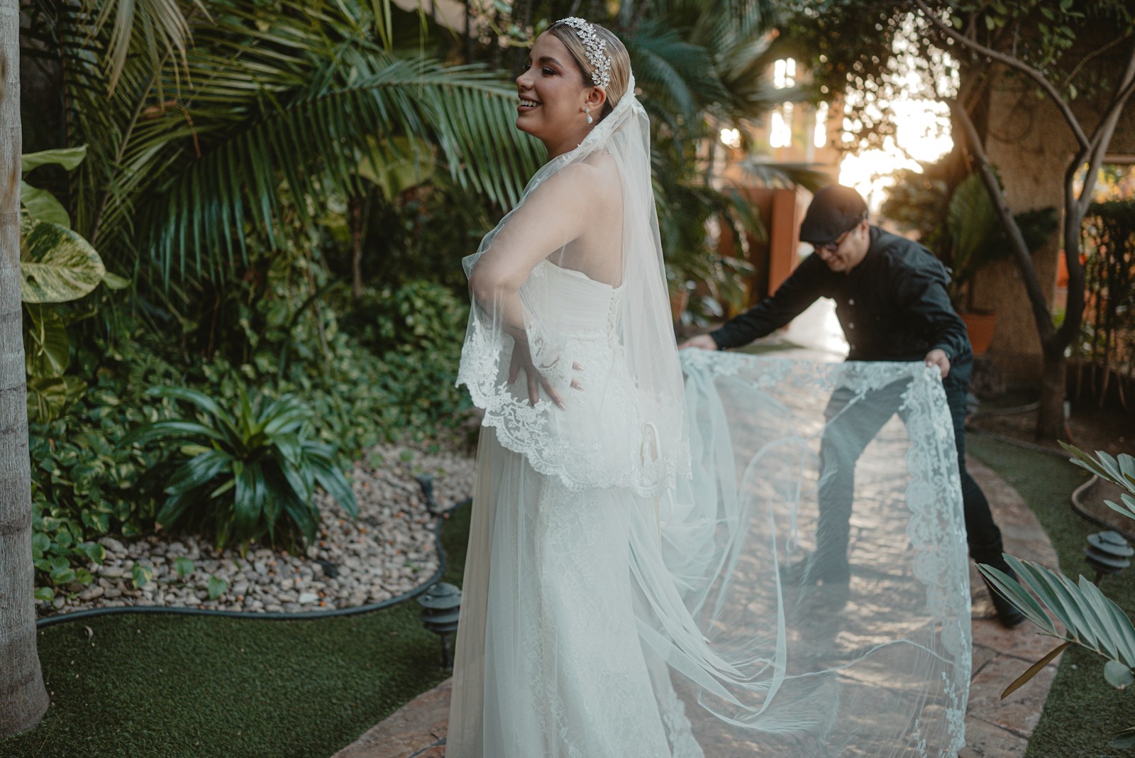 Bride in wedding dress with veil being adjusted outdoors