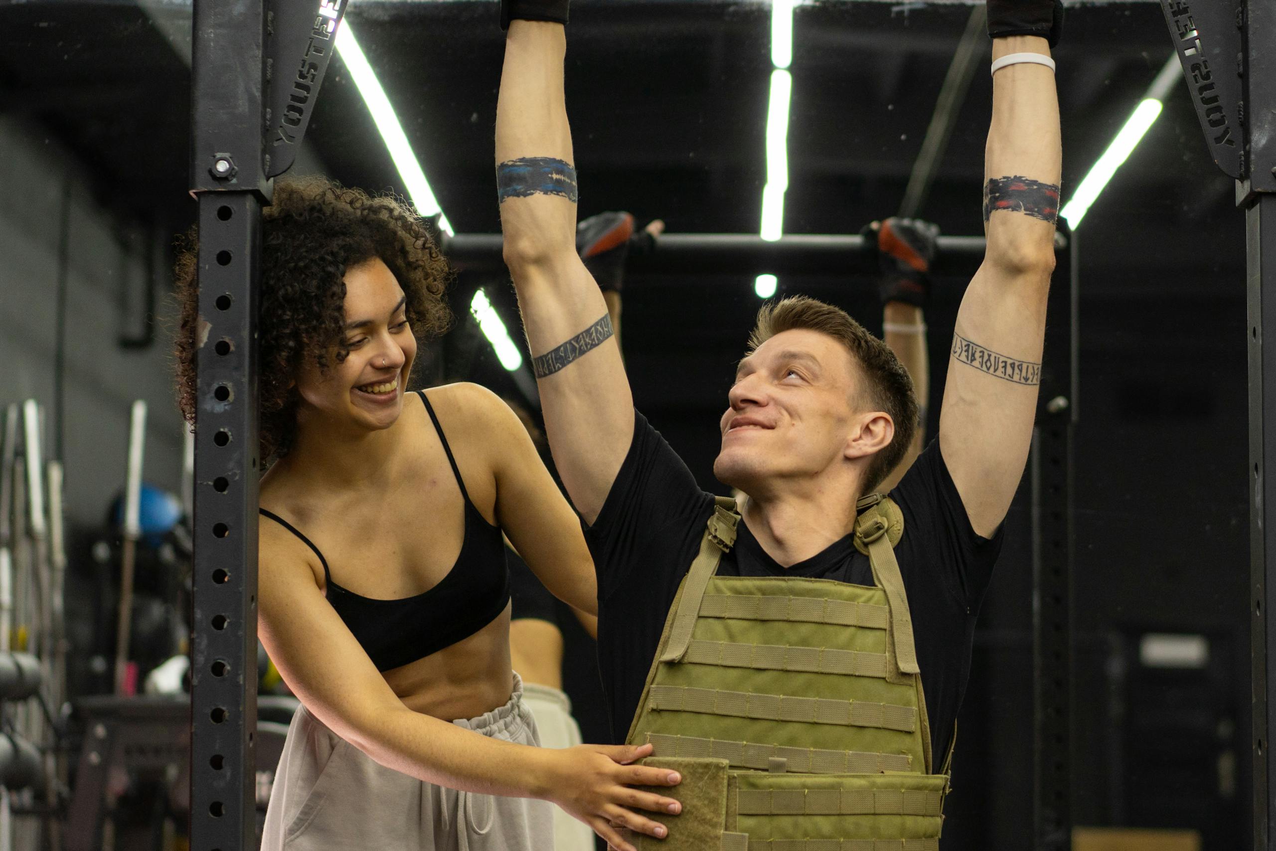 Personal trainer assisting man during workout in gym with smile and encouragement.