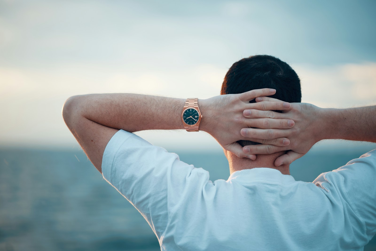 Man relaxing with hands behind head, watching the sea.
