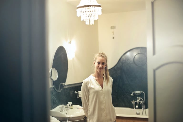 Portrait of a smiling woman in a stylish bathroom setting, showcasing luxurious decor and ambient lighting.