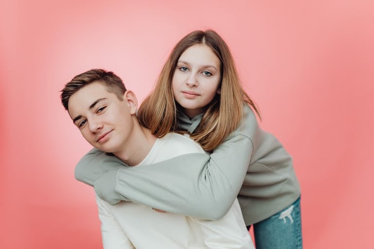 Portrait of two teenagers with arms around each other, smiling indoors.