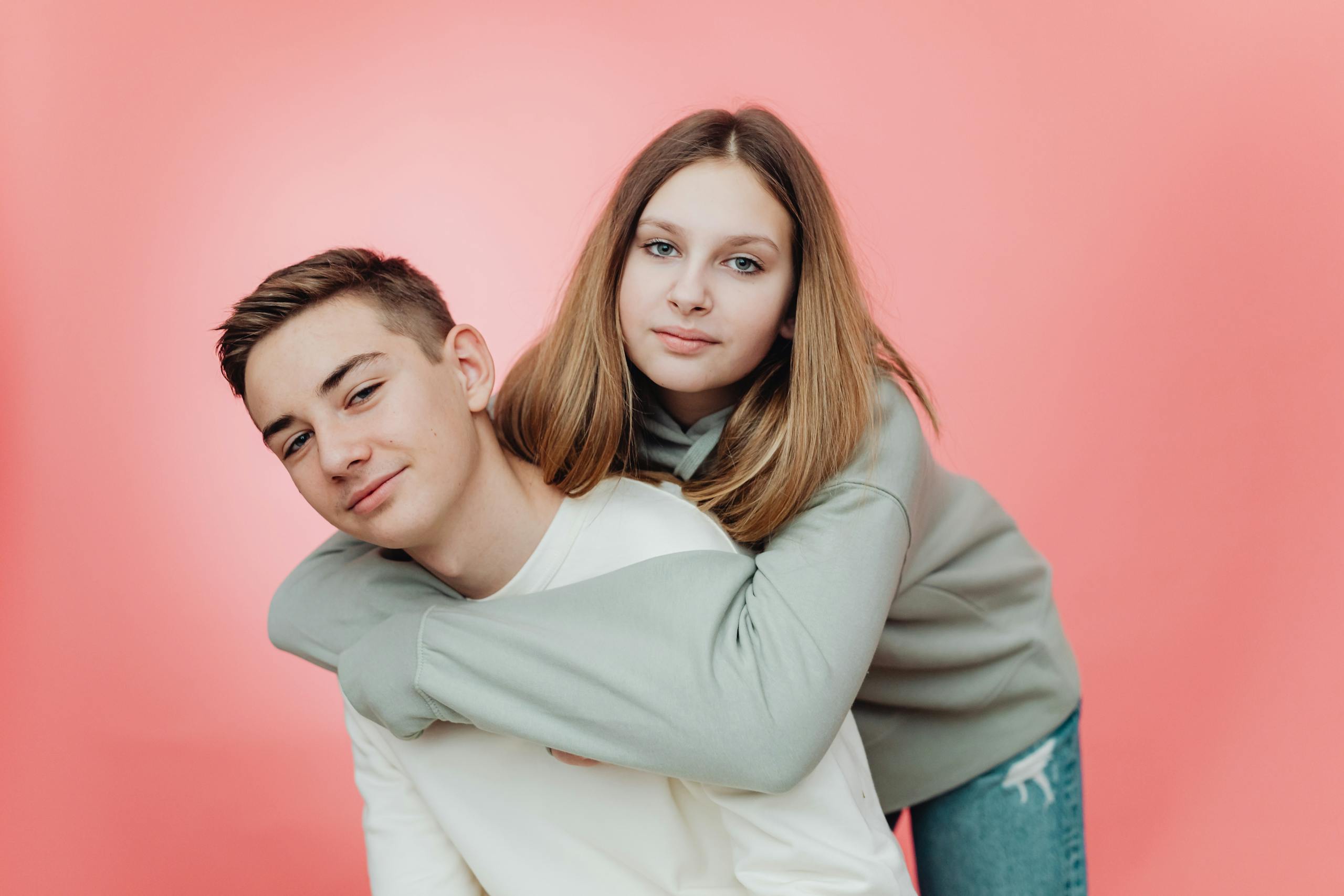 Portrait of two teenagers with arms around each other, smiling indoors.
