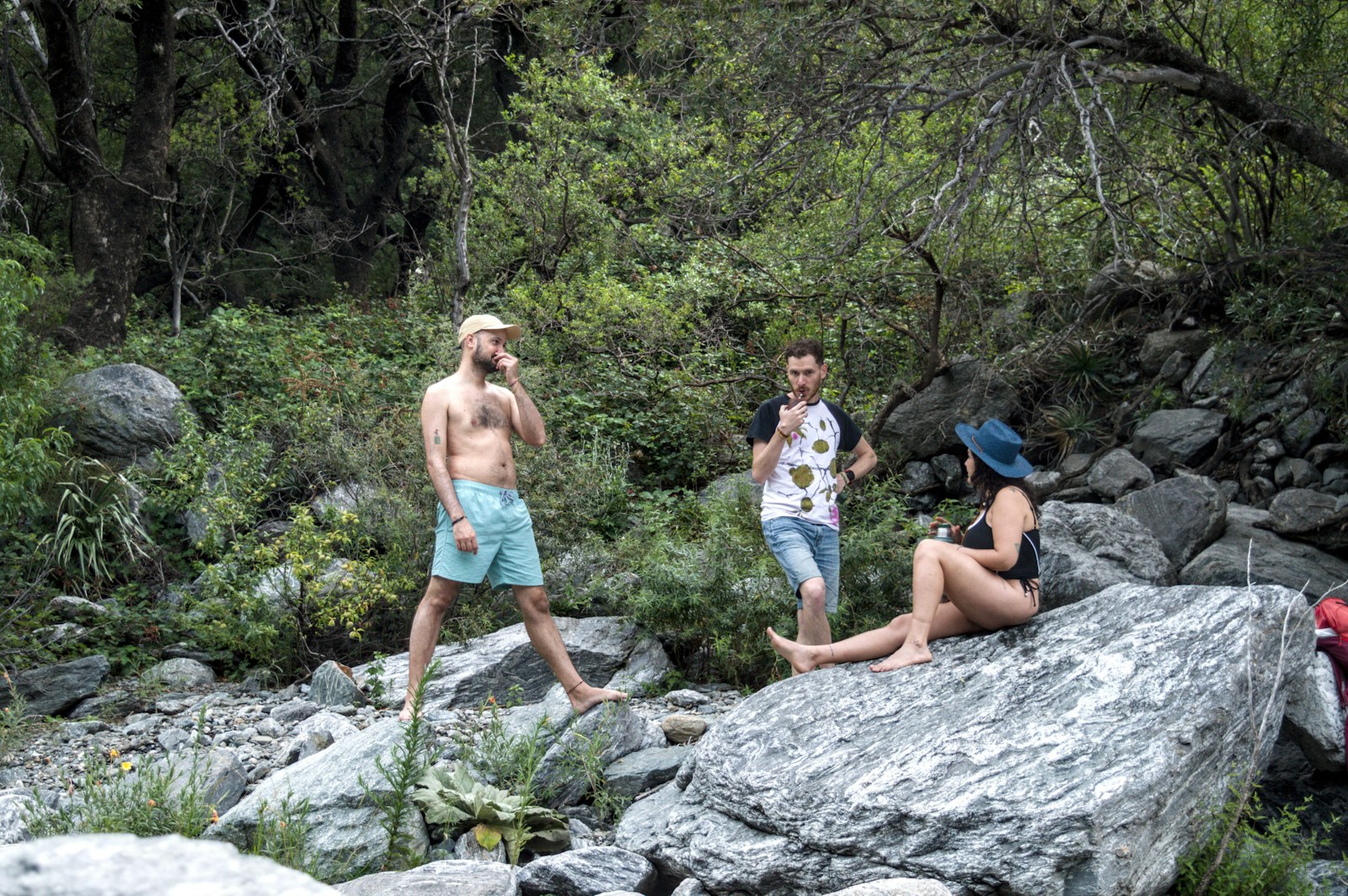 Three people relaxing by a rocky stream in a forest.
