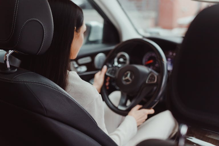 Rear view of a woman driving a Mercedes Benz, focusing on the interior and steering wheel.