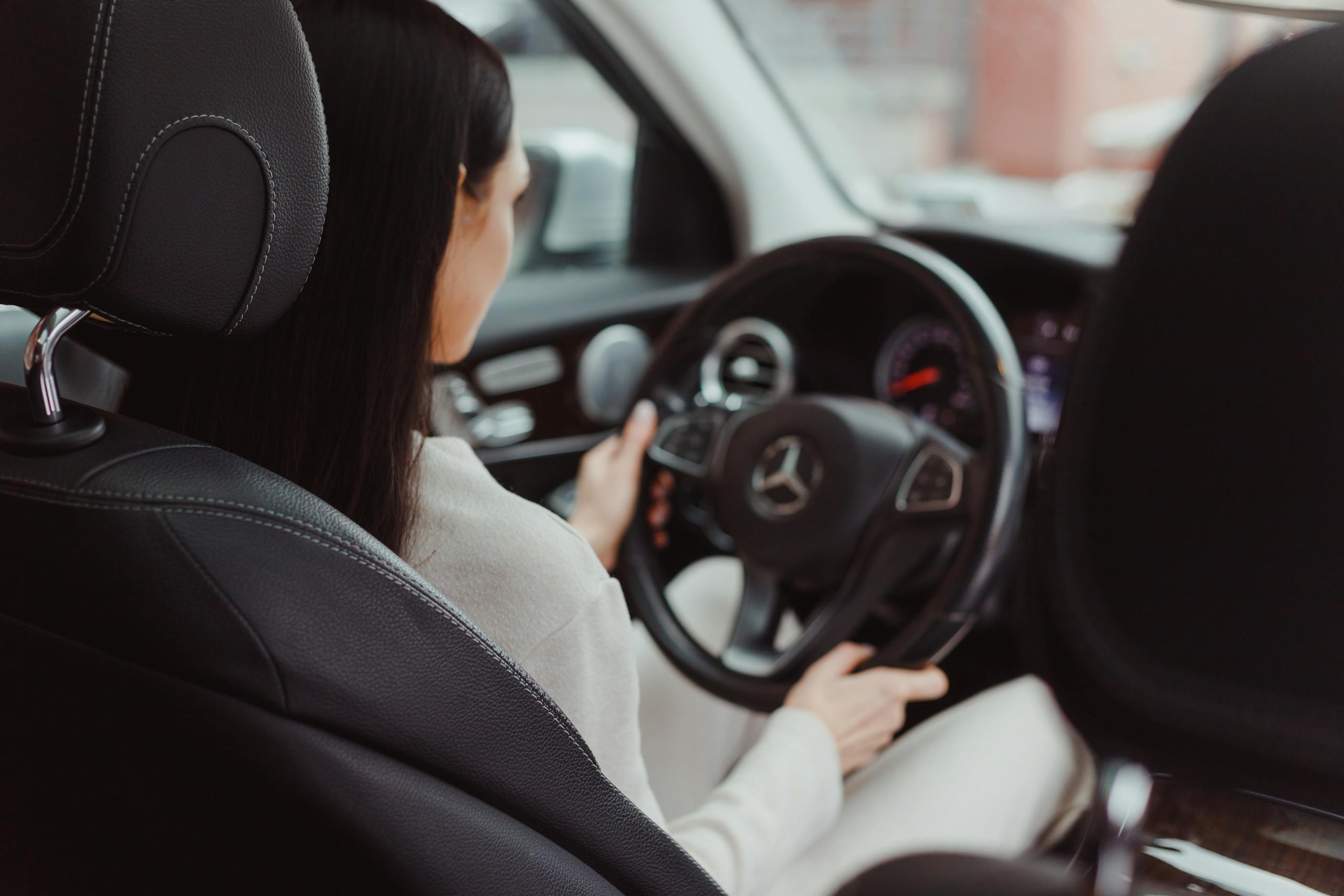 Rear view of a woman driving a Mercedes Benz, focusing on the interior and steering wheel.