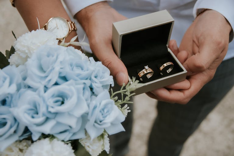 Romantic close-up of wedding rings in a box held with a bouquet of blue flowers, perfect for wedding themes.