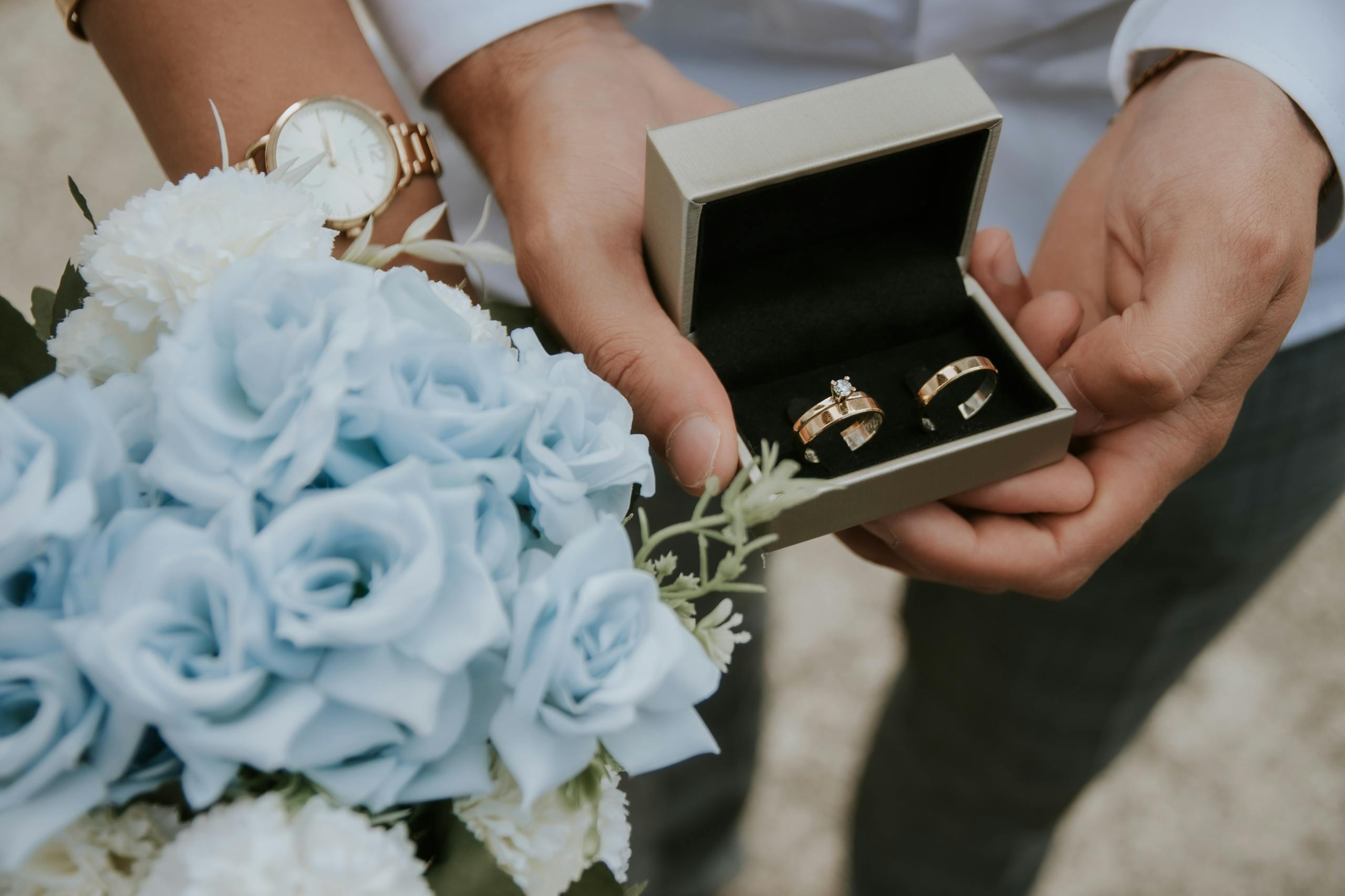 Romantic close-up of wedding rings in a box held with a bouquet of blue flowers, perfect for wedding themes.