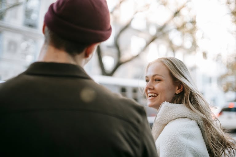 Smiling couple in outerwear standing in street near transport and building in daytime in town