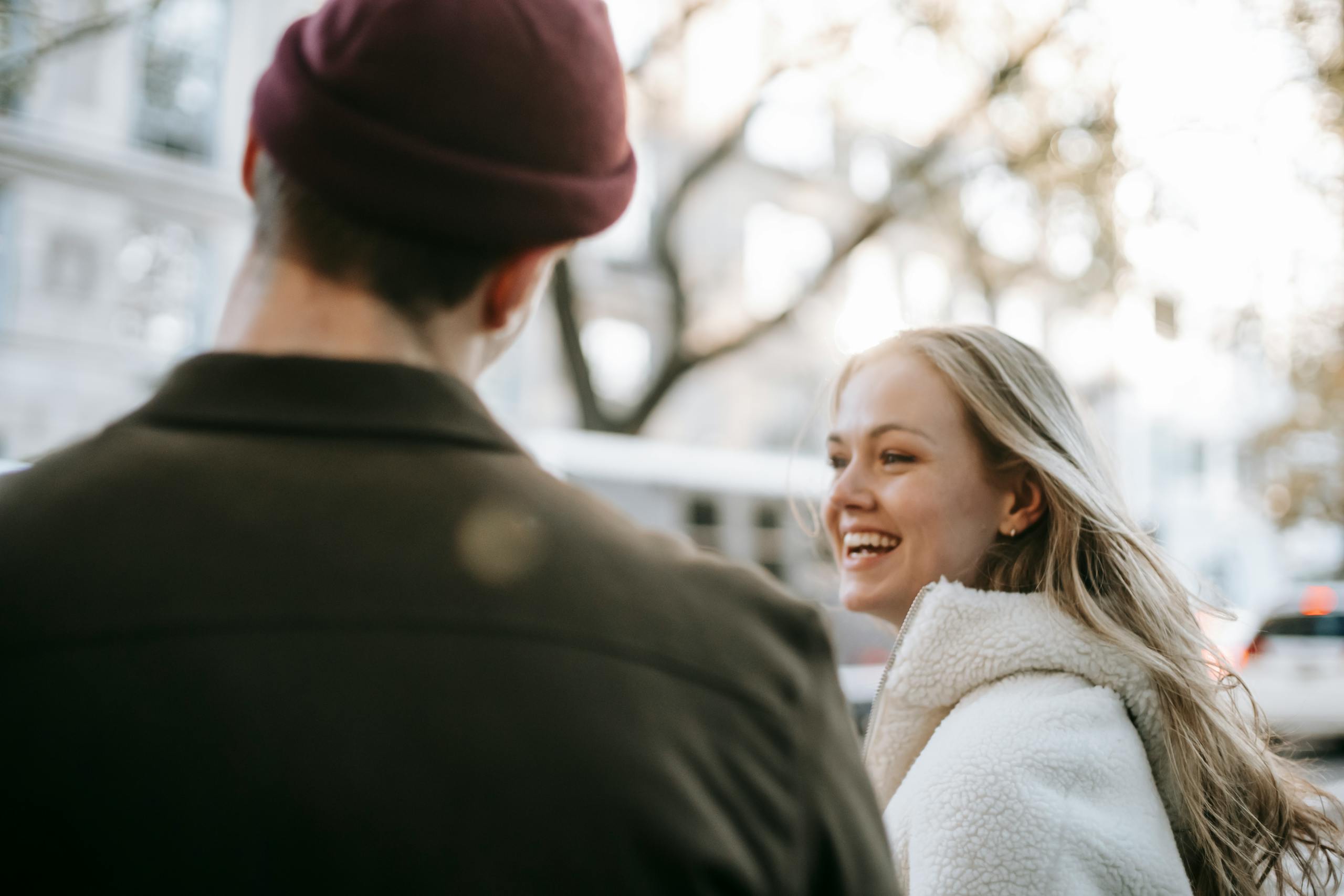 Smiling couple in outerwear standing in street near transport and building in daytime in town
