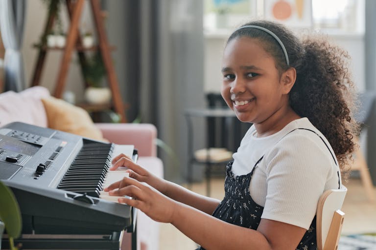Smiling girl enjoying playing the keyboard at home, creating a joyful musical atmosphere.