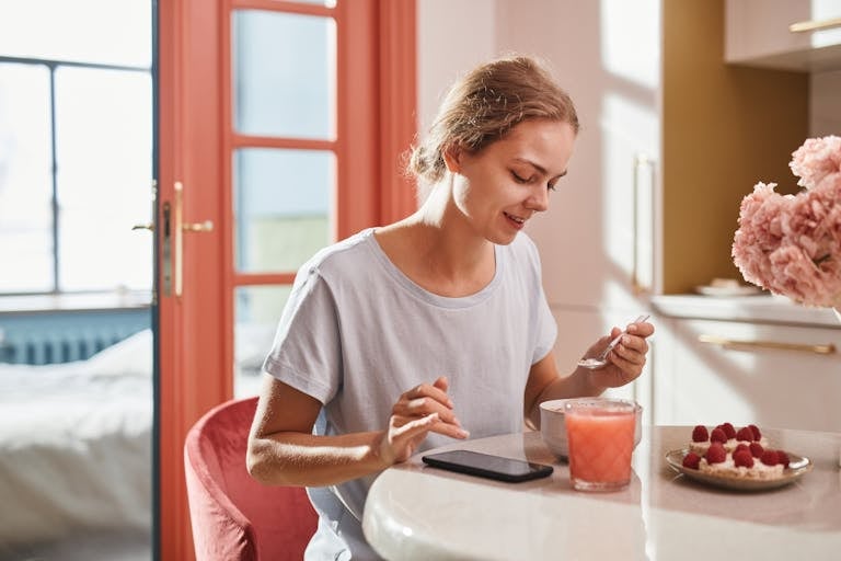 Smiling woman savoring a fresh breakfast with juice and dessert indoors.