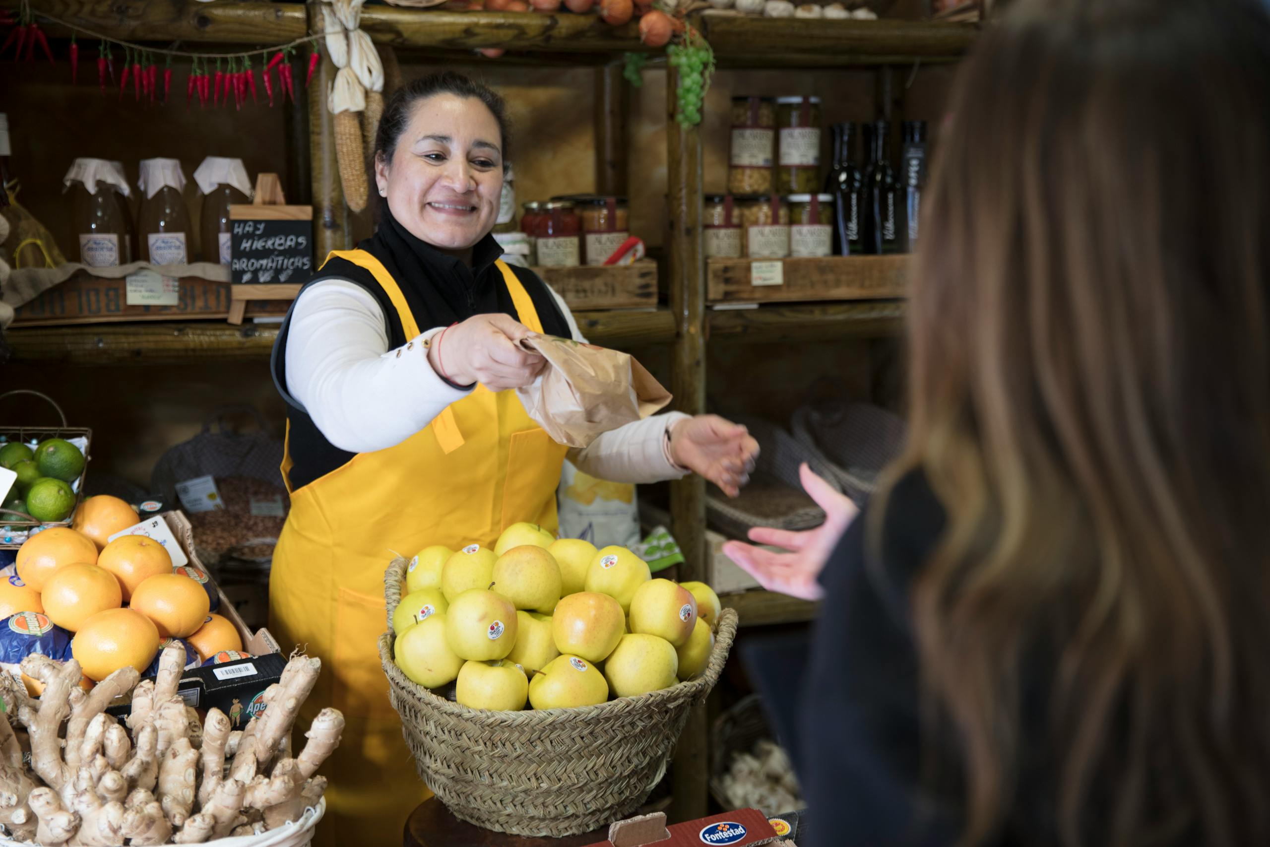 Smiling woman vendor handing a bag to a customer in a Madrid grocery store.
