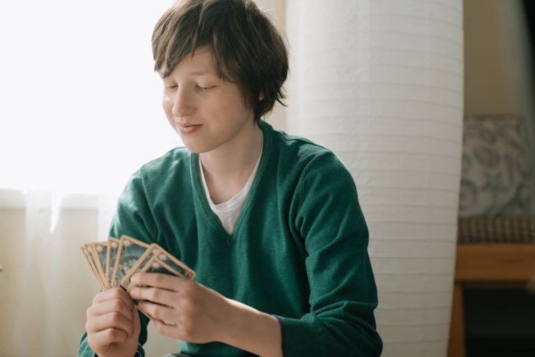 Teenager in green sweater smiling while playing a strategic card game indoors.
