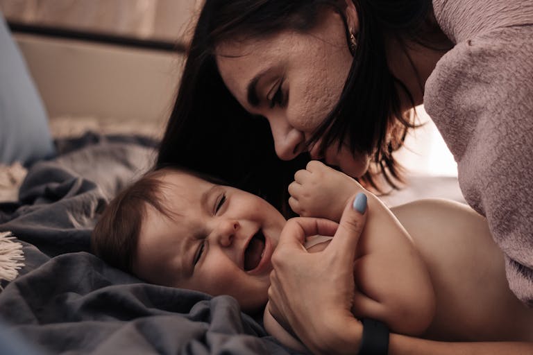 Tender moment between mother and baby, sharing a joyful laugh in a cozy indoor setting.