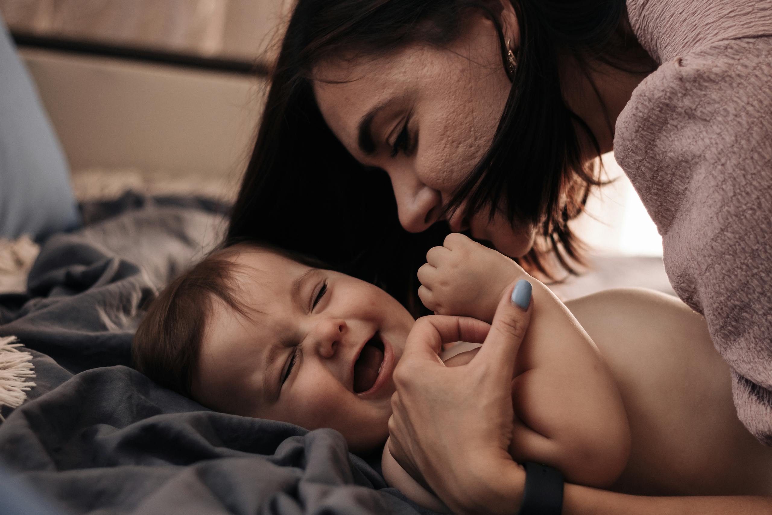 Tender moment between mother and baby, sharing a joyful laugh in a cozy indoor setting.