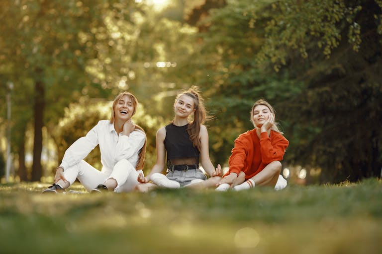 Three friends sitting on grass, enjoying a sunny outdoor day in the park.