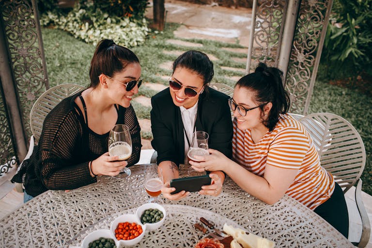 Three women sitting outdoors, sharing moments over drinks. Captured in a garden setting.
