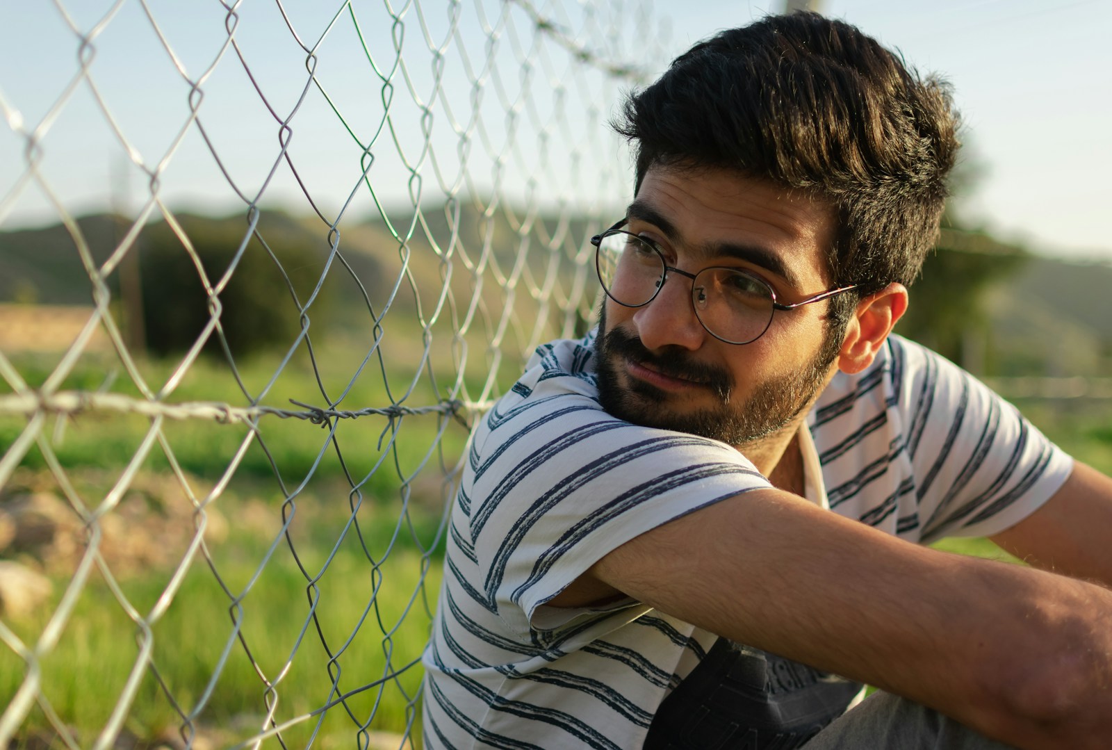 man in white and black striped shirt leaning on chain link fence