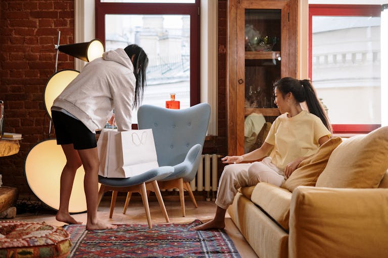 Two friends enjoying a cozy home environment while online shopping with a paper bag.
