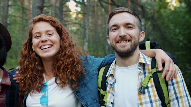 Two friends smiling during a forest hike, enjoying nature and friendship.