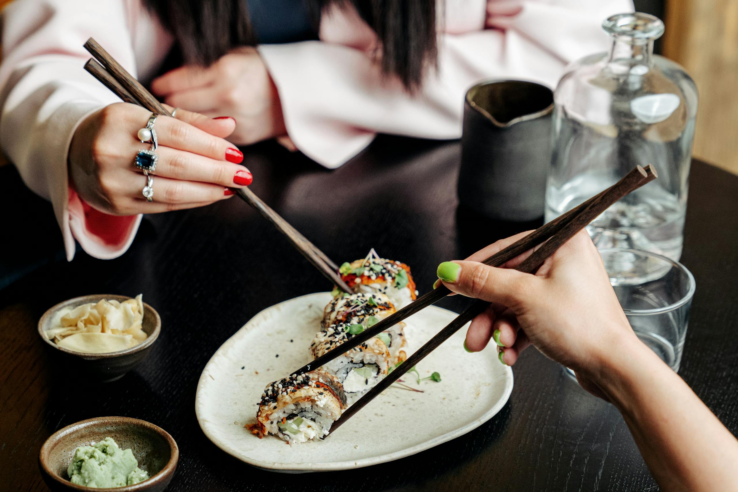 Two hands using chopsticks to enjoy sushi in a restaurant setting. Fresh and inviting Japanese cuisine.