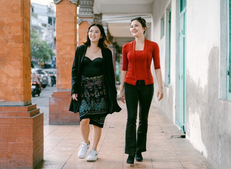 Two smiling women walk down an urban sidewalk, enjoying a sunny day in the city.