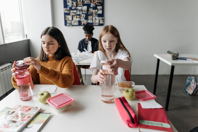 Two students with water bottles and snacks, enjoying a break in a classroom setting.