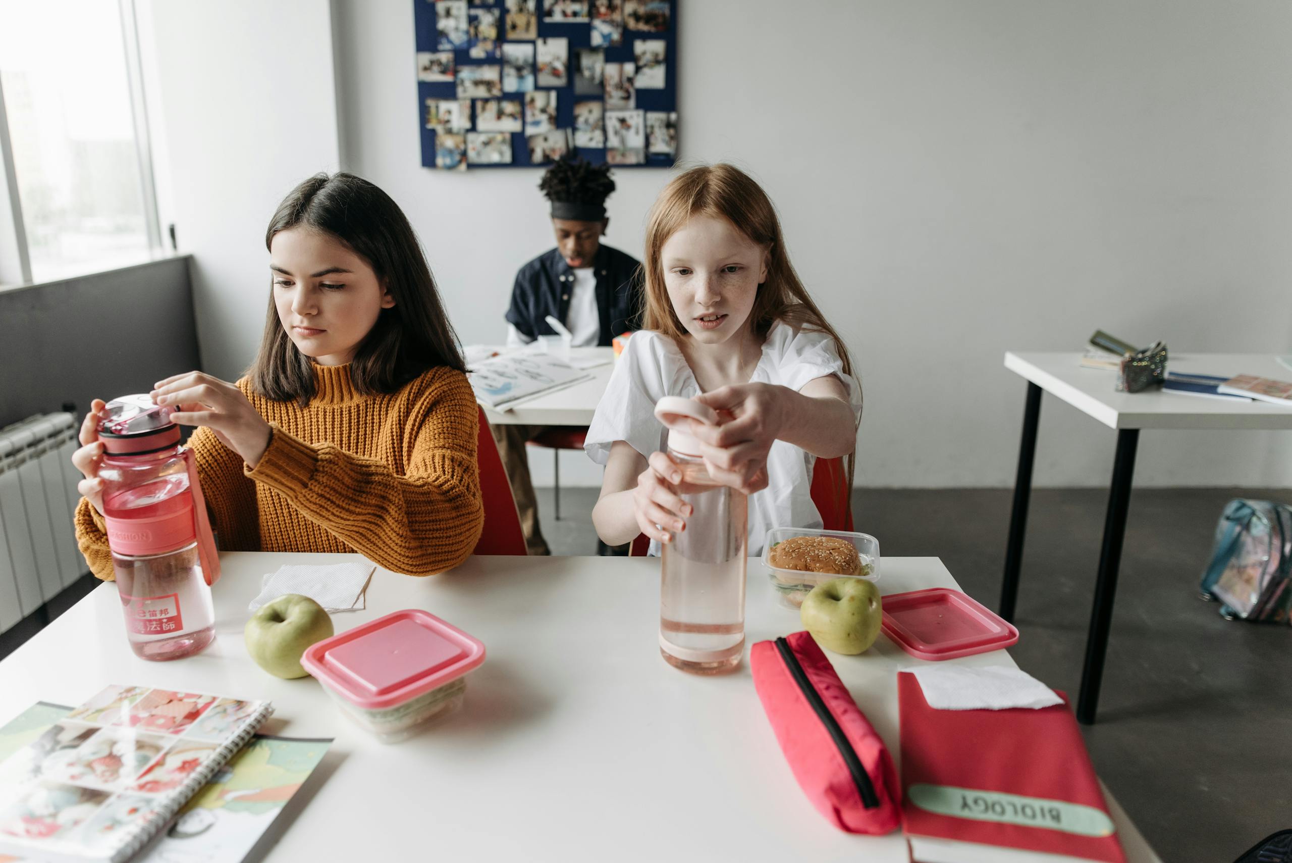 Two students with water bottles and snacks, enjoying a break in a classroom setting.