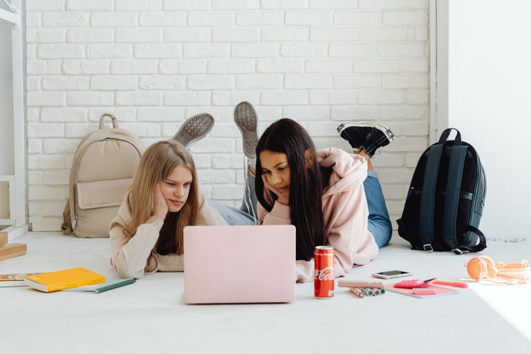 Two teenage girls studying together indoors, using a laptop on the floor.