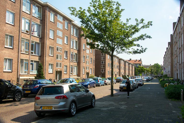 Urban street with parked cars and residential buildings on a sunny day.
