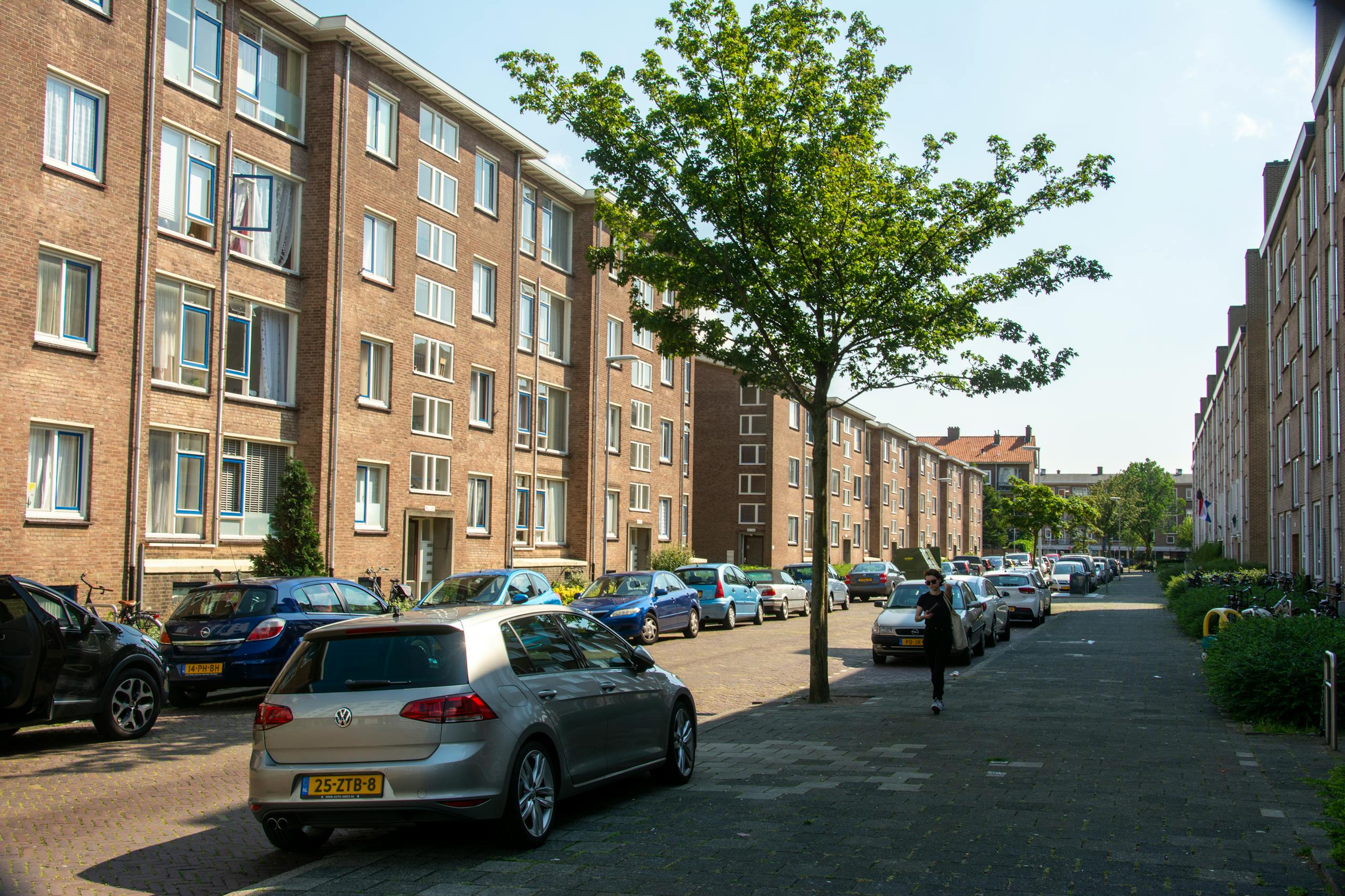 Urban street with parked cars and residential buildings on a sunny day.