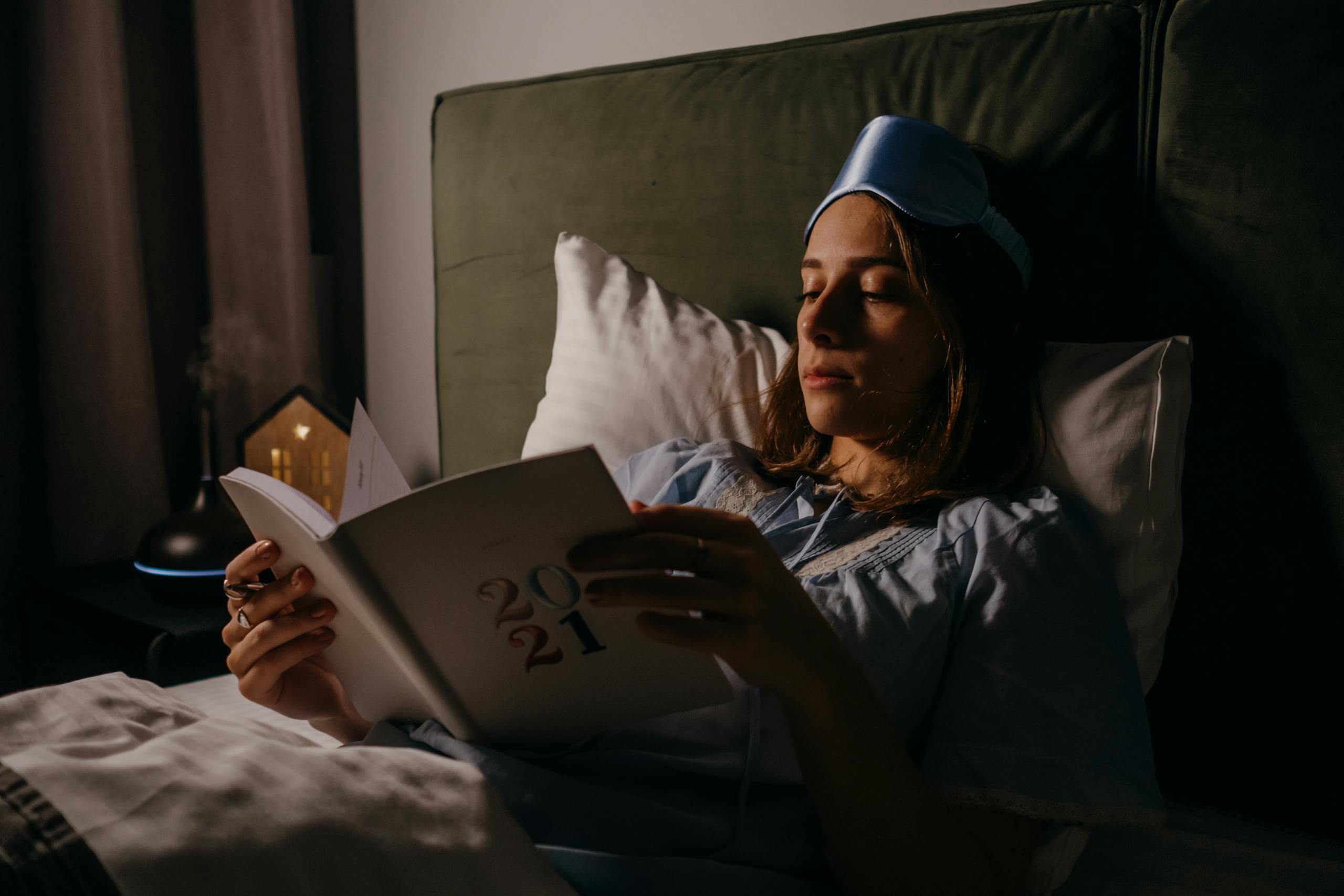 Woman in bed with sleep mask, reading a book, creating a relaxing, cozy atmosphere.